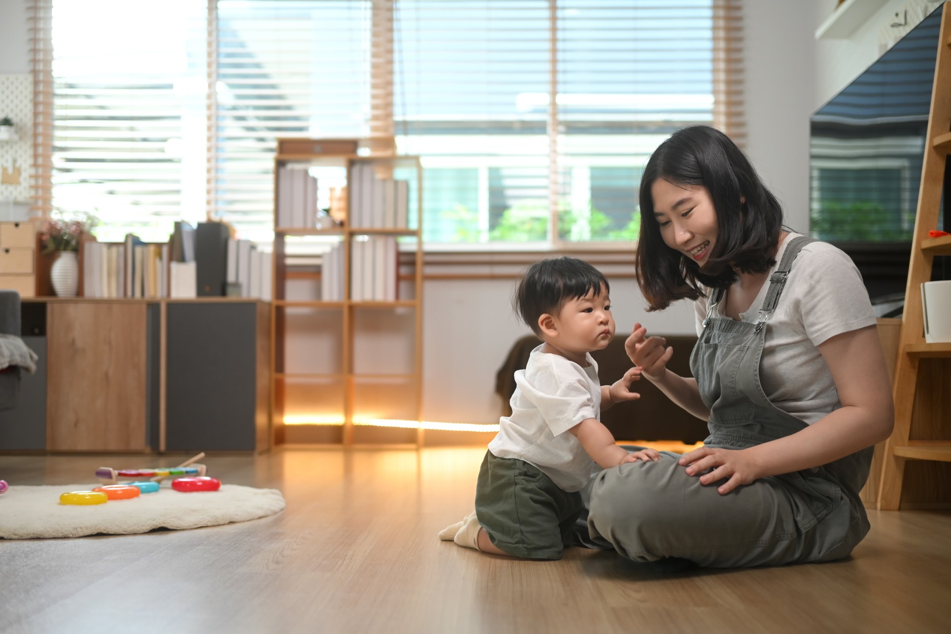 Happy young mother playing cute little boy on floor at home. Childhood and nurturing care concept